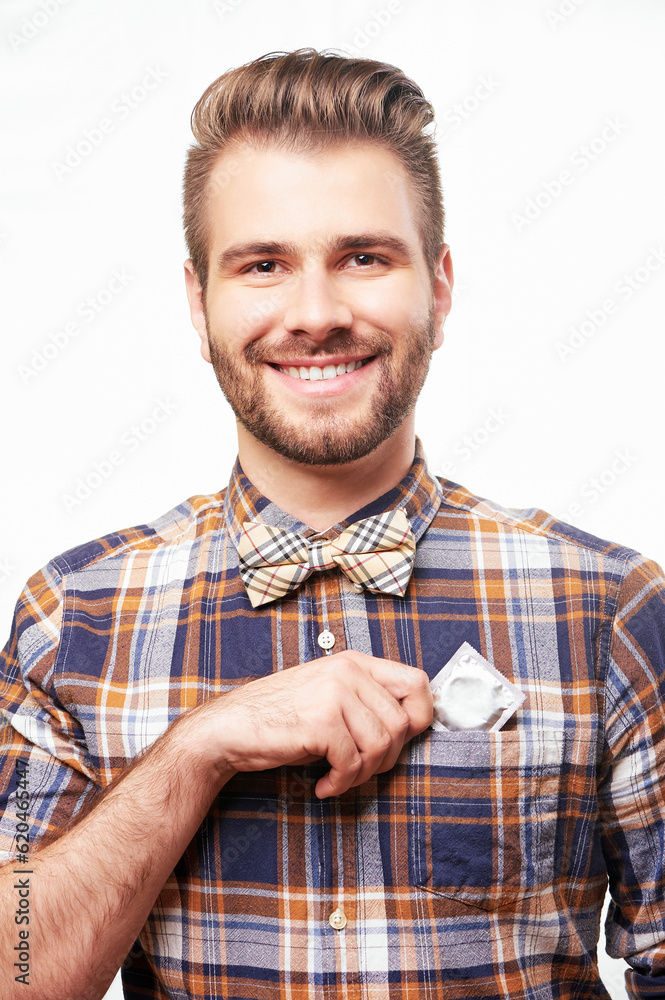Young handsome smiling man putting a condom into his shirt pocket. Isolated on white background. Young handsome smiling man putting a condom into his shirt pocket. Isolated on white background.