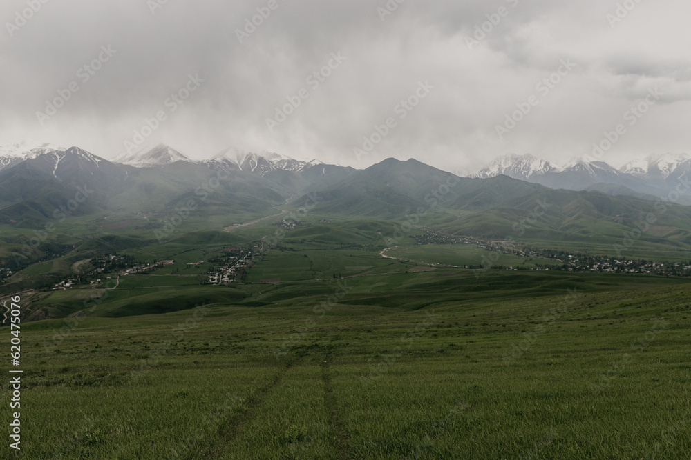 A summer view of mountain peaks shrouded in clouds and a distant village