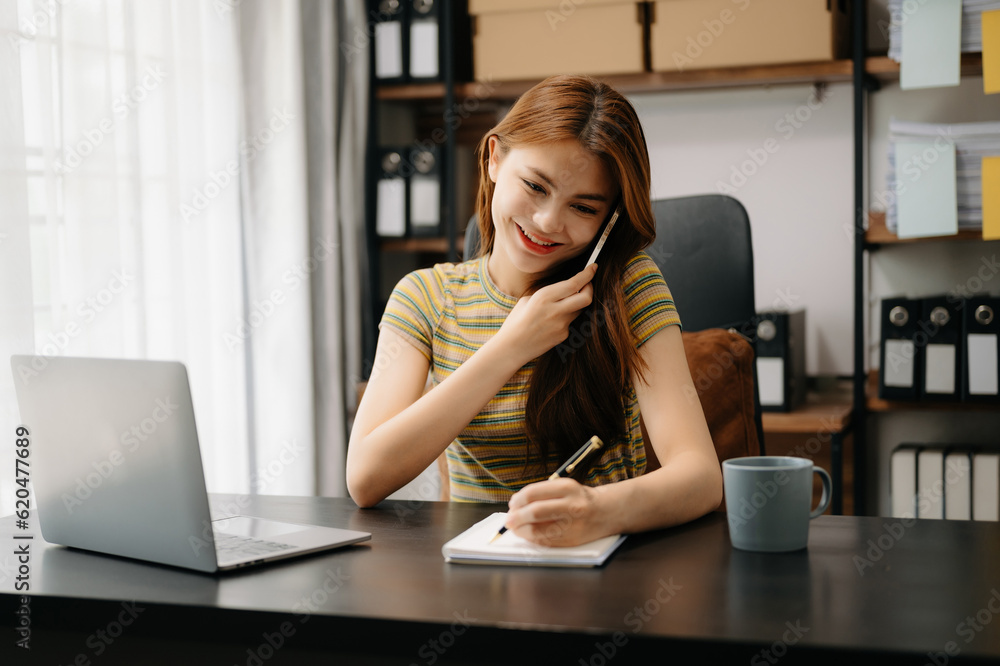 Business asian woman Talking on the phone and using a laptop with a smile while sitting at home office. Business asian woman Talking on the phone and using a laptop with a smile while sitting at home office.