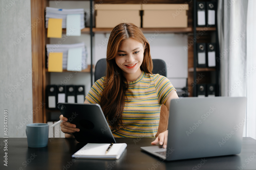 Business asian woman Talking on the phone and using a laptop with a smile while sitting at home office. Business asian woman Talking on the phone and using a laptop with a smile while sitting at home office.
