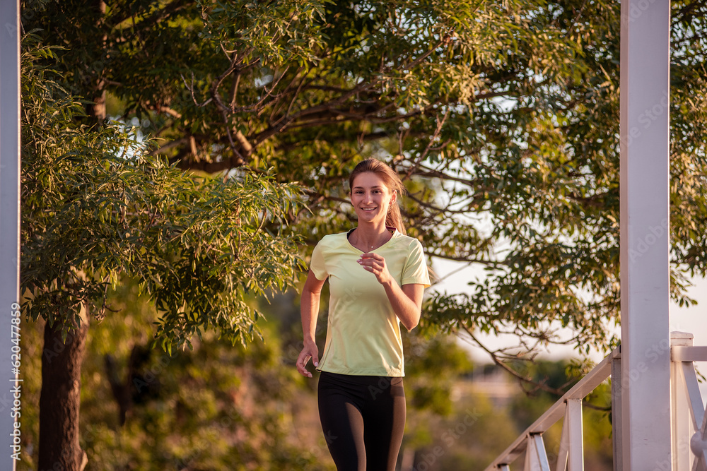 Young woman in sportswear is exercising, jogging on wooden stairs in the rays of the dawn sun. Going in for sports on street of the city. Girl posing in the concept of sport, fitness. Morning routine