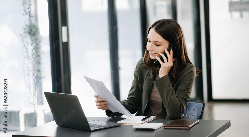 Business Caucasian woman Talking on the phone and using a laptop with a smile while sitting at modern office Business Caucasian woman Talking on the phone and using a laptop with a smile while sitting at modern office