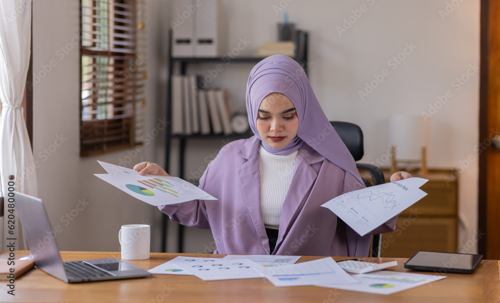 A stressed Asian business asian islamic woman in hijab holding documents is working from home, feeling stressed because of lot of paperwork appearing worried, tired, and overwhelmed A stressed Asian business asian islamic woman in hijab holding documents is working from home, feeling stressed because of lot of paperwork appearing worried, tired, and overwhelmed