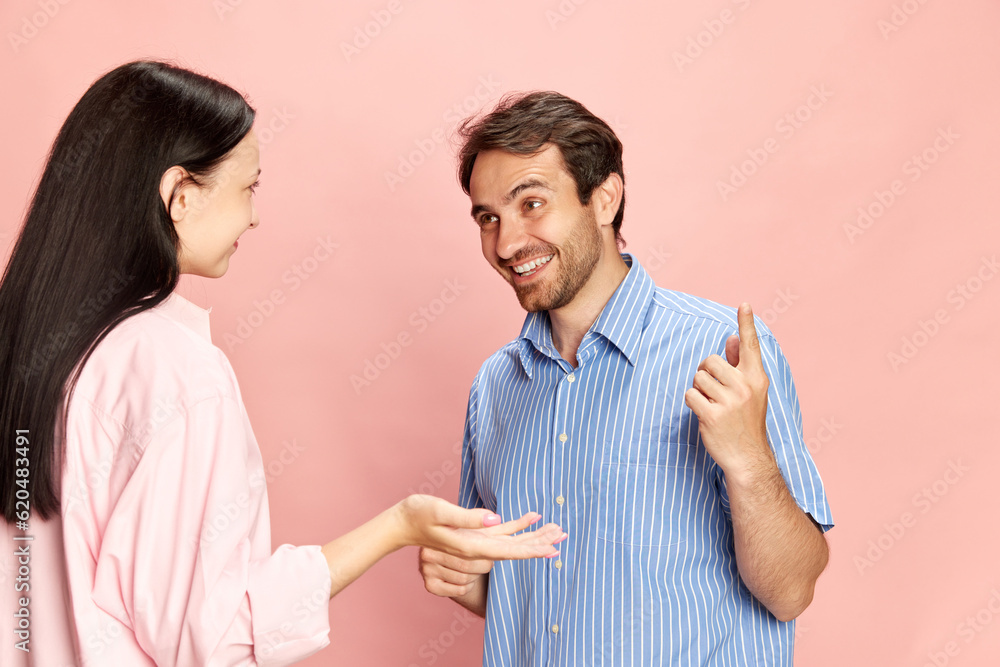 Positive smiling man talking to woman, discussing news and rumors against pink studio background. Lively conversation. Concept of friendship, relationship, communication, emotions, lifestyle, ad Positive smiling man talking to woman, discussing news and rumors against pink studio background. Lively conversation. Concept of friendship, relationship, communication, emotions, lifestyle, ad