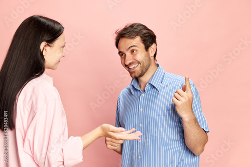 Positive smiling man talking to woman, discussing news and rumors against pink studio background. Lively conversation. Concept of friendship, relationship, communication, emotions, lifestyle, ad