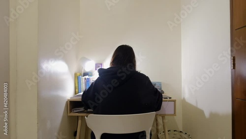 Static wide shot of girl with black hair in jacket sitting and studying at desk. photo