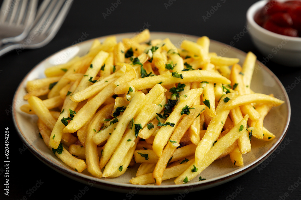 Garlic French Fries with Parsley on a Plate on a black background, side view. Close-up. Garlic French Fries with Parsley on a Plate on a black background, side view. Close-up.