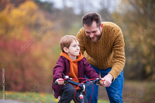 Father teaching his little son to ride bicycle in park. Bearded man helping child to learn bike. Family values, child support, fathers day concept. Selective focus. © Natallia