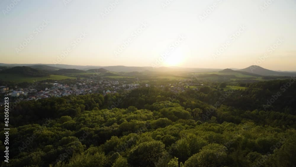 Tree crowns of a thick forest with a town in the background during sunset - top view