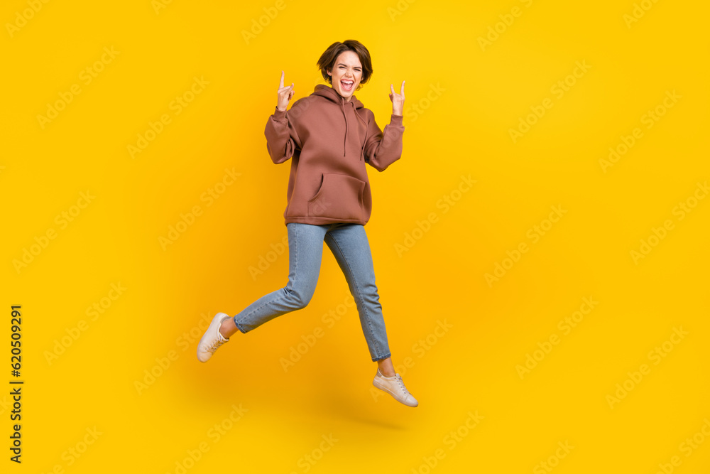 Full body photo cadre of young crazy brutal girl jump wear brown sweatshirt show metal punk rock sign isolated on yellow color background
