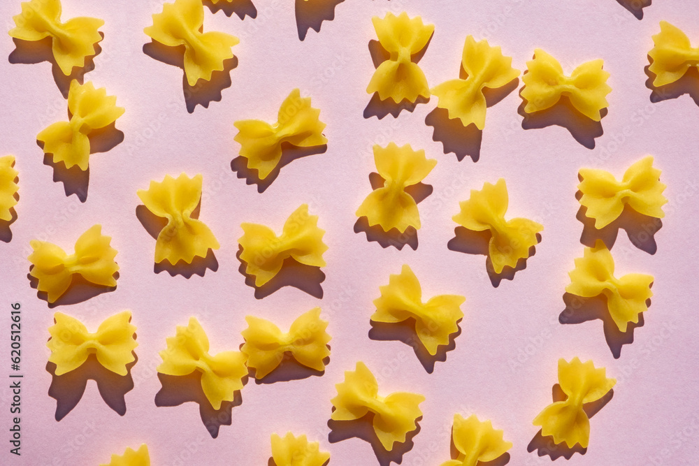 Fototapeta premium Farfalle pasta pile on pastel pink surface. Cute shape of raw, uncooked pasta on blight pink background. Italian cuisine.