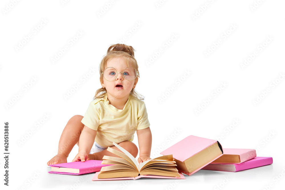 Smart, curious baby. Little girl, toddler sitting on floor with many books around against white studio background Smart, curious baby. Little girl, toddler sitting on floor with many books around against white studio background