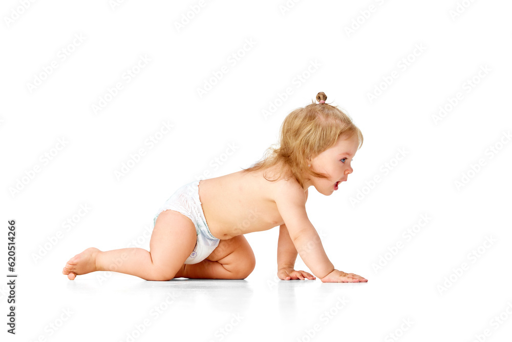 Side view. Beautiful, little, baby girl, toddler in diaper crawling on floor, playing against white studio background Side view. Beautiful, little, baby girl, toddler in diaper crawling on floor, playing against white studio background