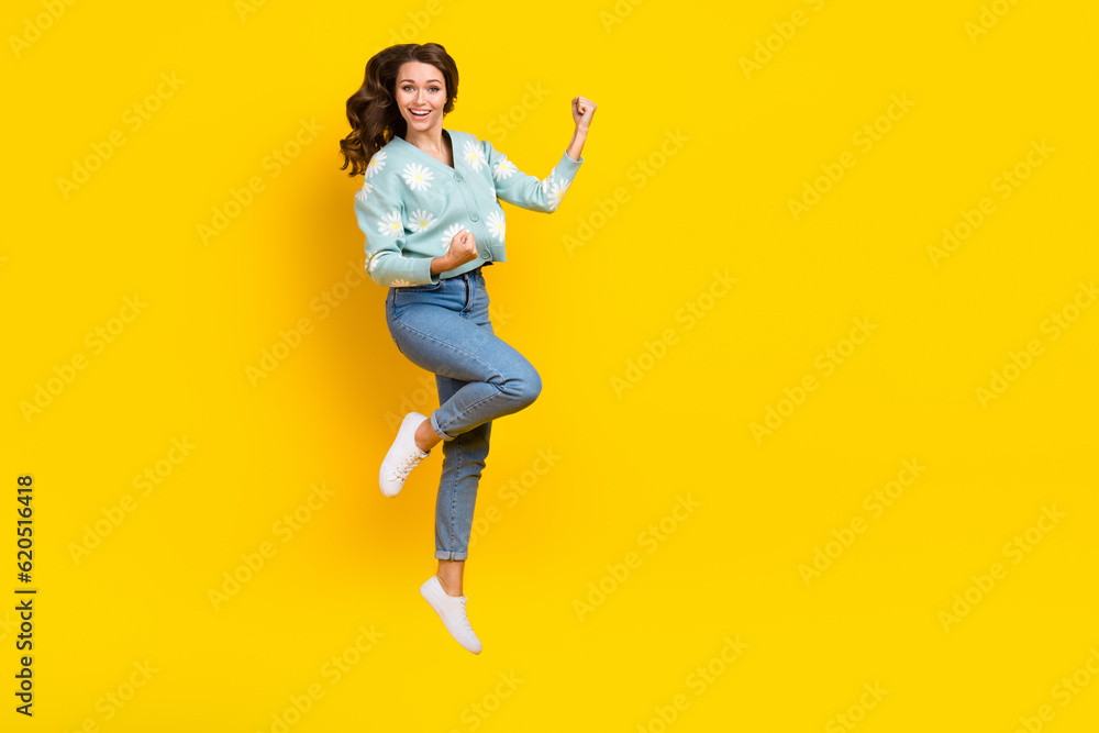 Full length portrait of delighted pretty person jumping raise fists achieve isolated on yellow color background Full length portrait of delighted pretty person jumping raise fists achieve isolated on yellow color background
