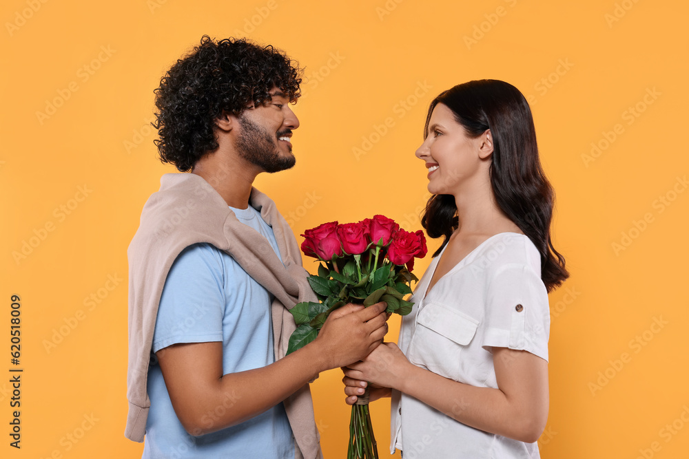 International dating. Happy couple with bouquet of roses on yellow background International dating. Happy couple with bouquet of roses on yellow background