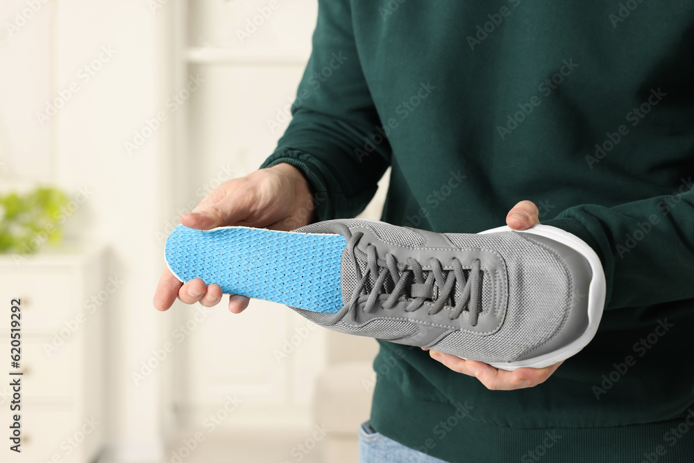 Obraz premium Man putting orthopedic insole into shoe indoors, closeup