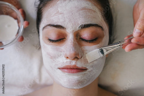 Close up portrait of a young woman having a facial white mask on her face in a spa salon.
