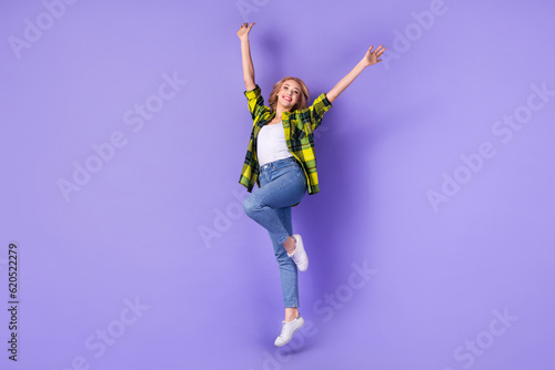 Full body photo of woman curly hair active weekend jump up high raised hands wear plaid stylish shirt isolated on violet color background