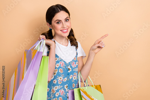 Photo of young marketer girl wear stylish overall point finger empty space hold bags from bershka brand isolated on beige color background photo