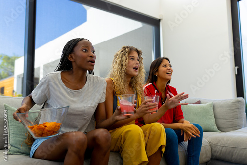 Group of excited diverse female friends sitting on sofa, watching sport on tv #620528614