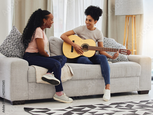 Guitar, happy or women in house for music, social or entertainment while laughing together on sofa. Smile, acoustic or creative musician friends with an instrument for artistic expression in a home photo