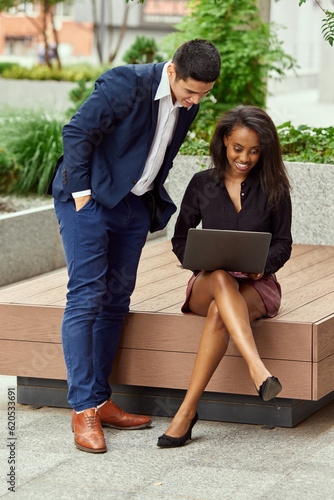 Young man and woman, employees working together on business project, sitting outside the office and discussing work