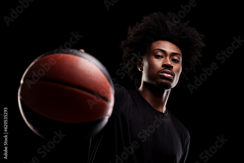 Basketball player holding a ball at camera. Shallow focus. Young african american sports man against black background.