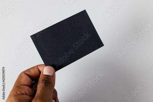 Hand of biracial man holding black business card with copy space on white background
