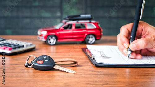 Car loan or buying a new car concept. Car key on table with a man signing on leasing or document  form and red car in background. Leasing and insurance business.