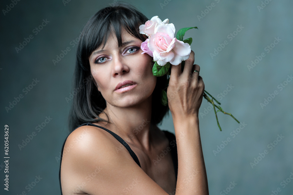 Beautiful brunette woman with flower in black bodysuit posing in a dark background