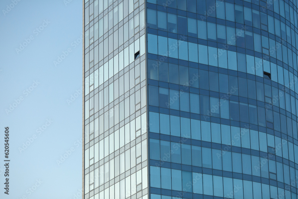 Part of a glass mirrored office building reflecting the blue sky.