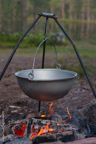 a camp pot hangs over the fire on a tripod. Cooking on a camping trip, hiking