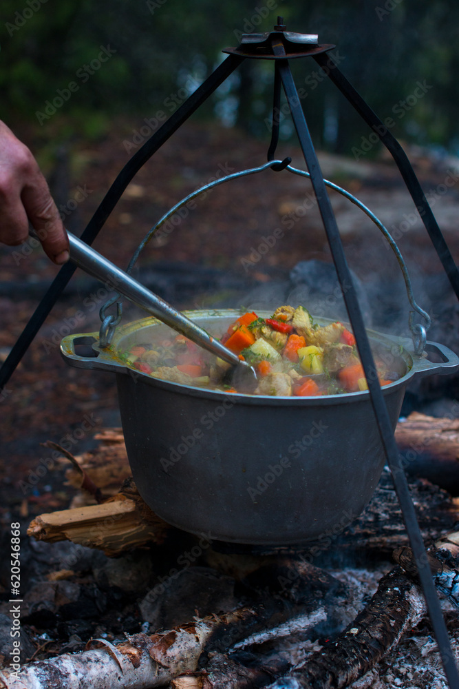 a camp pot hangs over the fire on a tripod. Cooking on a camping trip, hiking a camp pot hangs over the fire on a tripod. Cooking on a camping trip, hiking