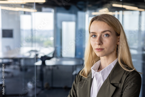 Free Download Portrait of a young confident blonde businesswoman in a suit standing in the office and smiling at the camera. Close-up photo - GFXLoad