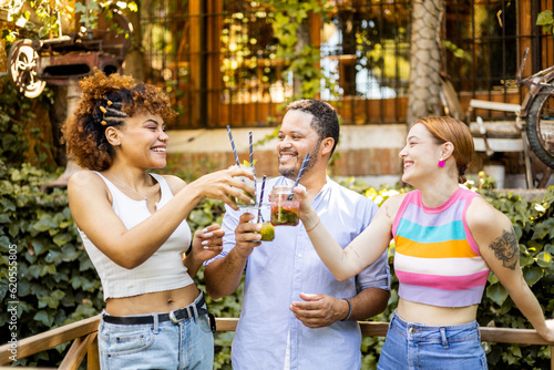 Wall Mural A group of 3 multi-ethnic young people celebrate summer by sipping cocktails on an outdoor bar terrace