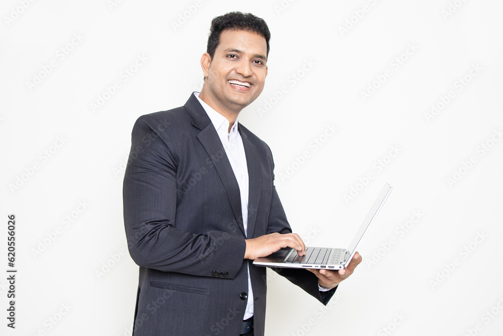 Smiling handsome young indian businessman wearing suit holding laptop isolated over white background. Corporate Concept. Smiling handsome young indian businessman wearing suit holding laptop isolated over white background. Corporate Concept.