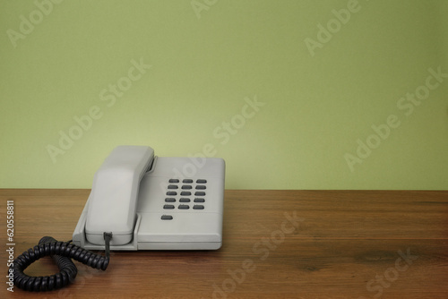 Grey retro style telephone with green background on wooden desk