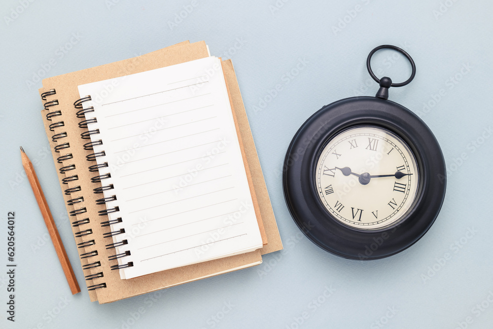 Empty white notebook on pile with a black vintage clock, writing and timing concept Empty white notebook on pile with a black vintage clock, writing and timing concept
