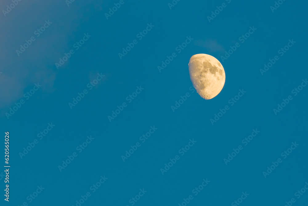 Bright sunlit moon in clear blue evening sky