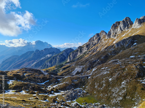 Alpine road over meadows under rocky peaks