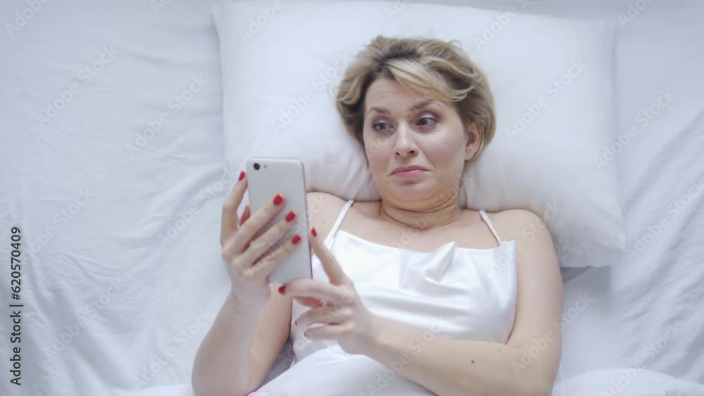 Business woman waking in her weekend morning, lying in bed and reading news on smartphone, controlling employees work distantly, checking statistics and reports Business woman waking in her weekend morning, lying in bed and reading news on smartphone, controlling employees work distantly, checking statistics and reports