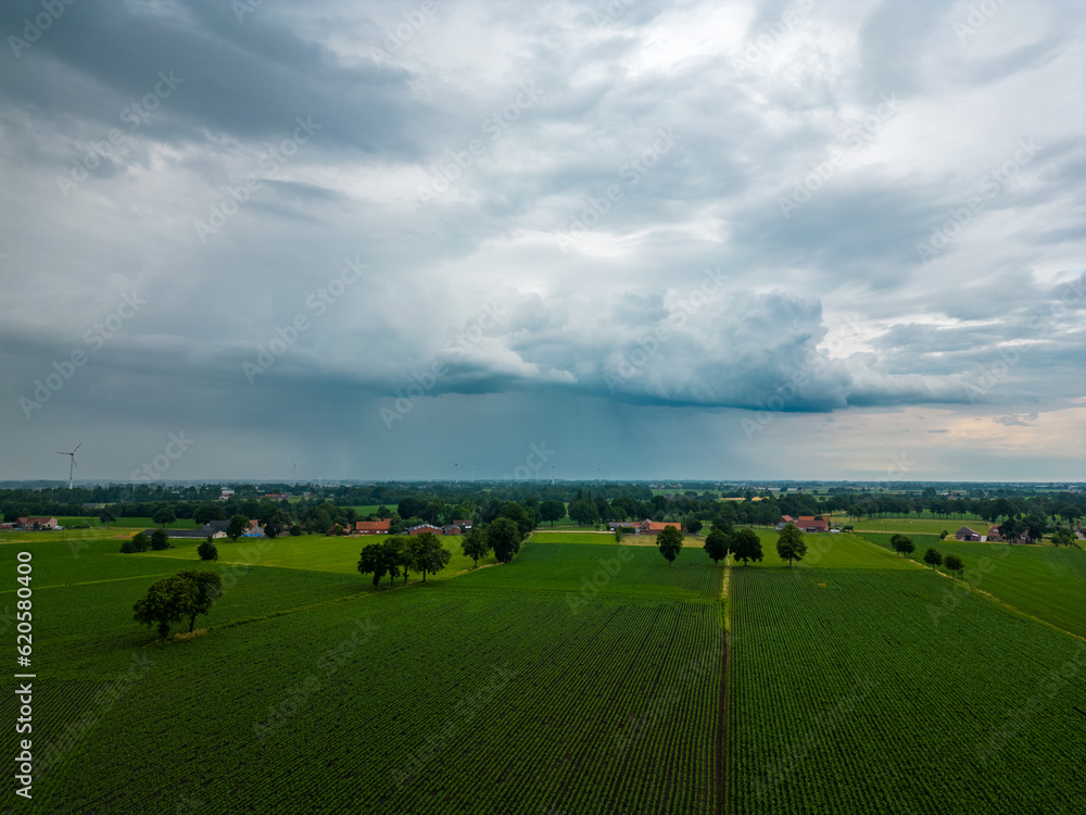 An awe-inspiring aerial shot capturing the menacing beauty of storm clouds brewing over serene farmland. The juxtaposition of the plain field against the backdrop of a dark, wind-swept sky creates a
