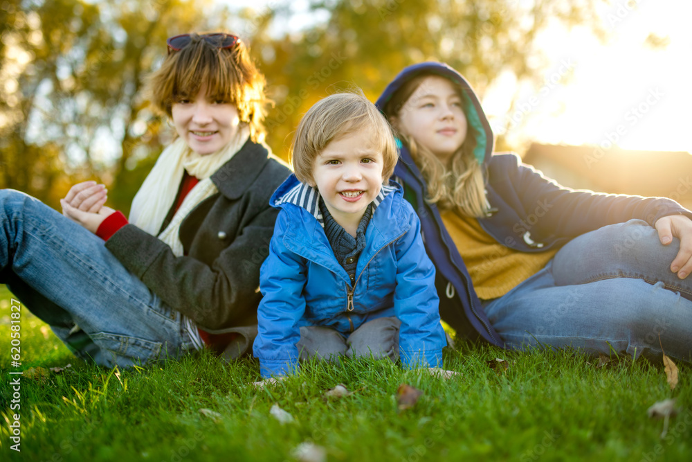 Fototapeta premium Two big sisters and their toddler brother having fun outdoors. Two young girls with a toddler boy on autumn day. Children with large age gap.