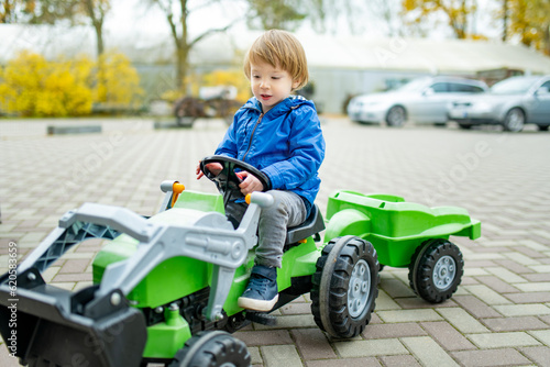 Adorable toddler boy riding his toy tractor in a city on sunny autumn evening. Young child riding a roller.