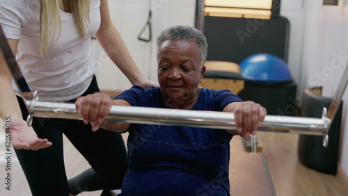 Photography Female Pilates Coach assisting a black senior woman to use machine, old age work