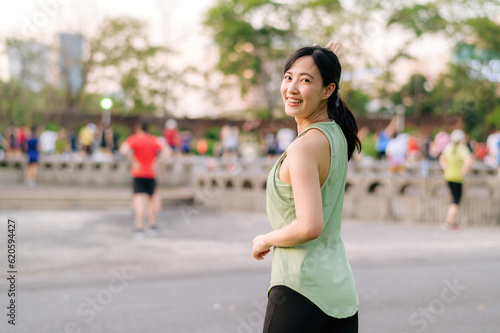 Female jogger. Fit young Asian woman with green sportswear aerobics dance exercise in park and enjoying a healthy outdoor. Fitness runner girl in public park. Wellness being concept