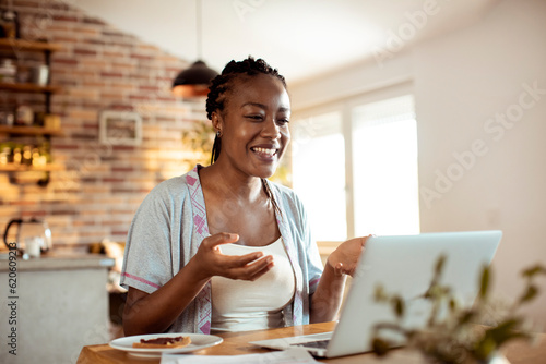 Young woman using a laptop in the morning while having breakfast in the kitchen