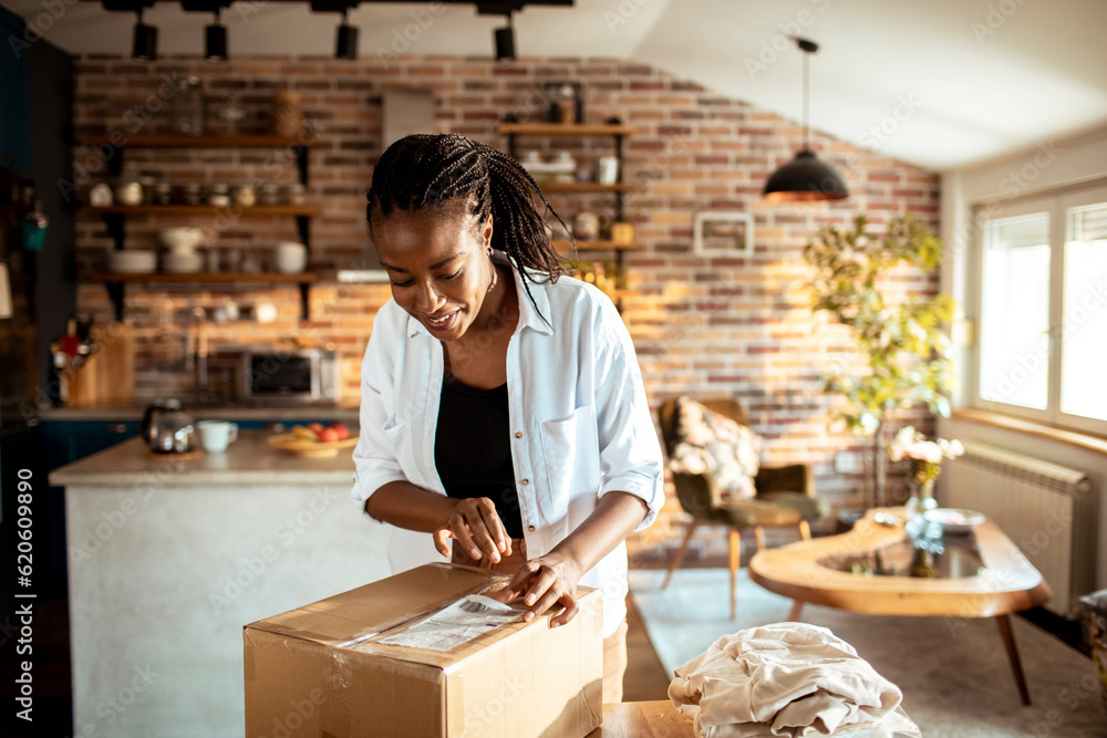 Young woman opening up the package she received in the mail at home in th ekitchen Young woman opening up the package she received in the mail at home in th ekitchen