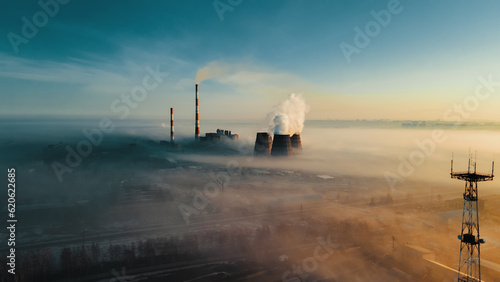 Chimneys of thermal power plant rise from fog on horizon line against sky. View of pipes from drone. Atmospheric photo of industrial area from above in smoke and fog.
