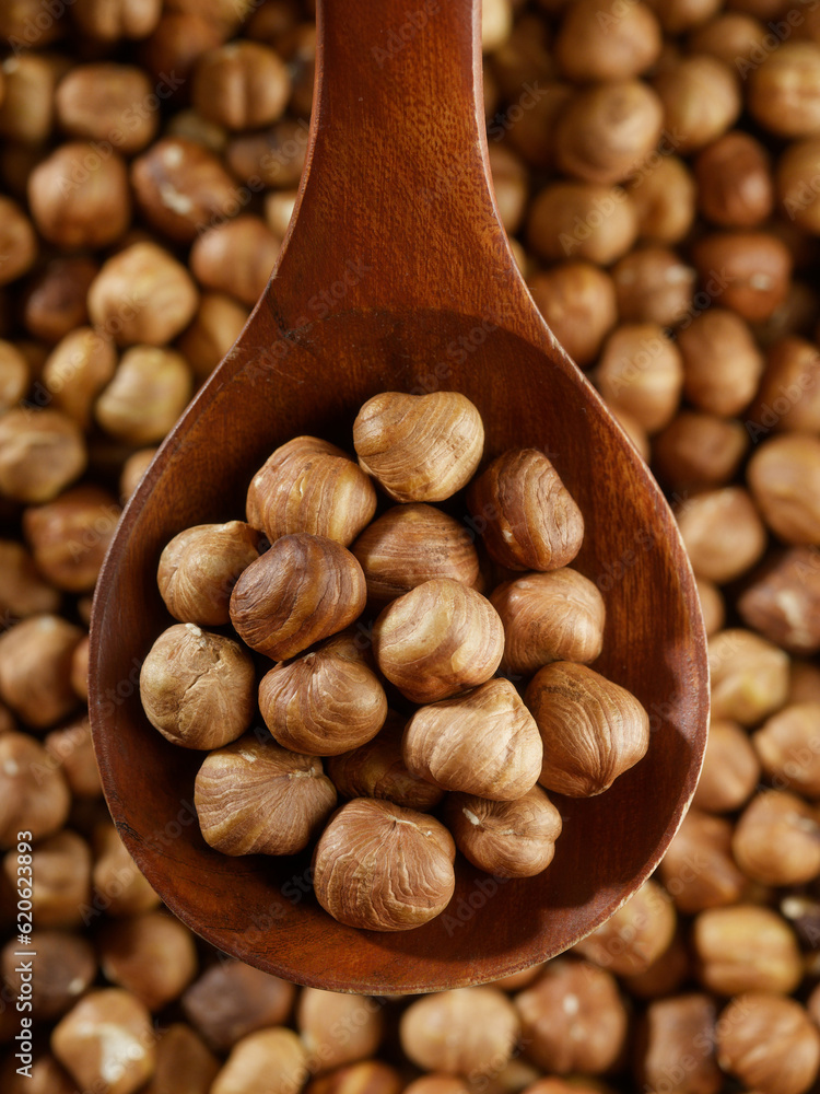 Fototapeta premium Peeled hazelnuts in close-up with wooden spoon. View from above. Promotional photo of healthy nut for online store and marketplaces.